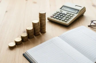 Столбики монет ступеньками, калькулятор, тетрадь и очки на столе